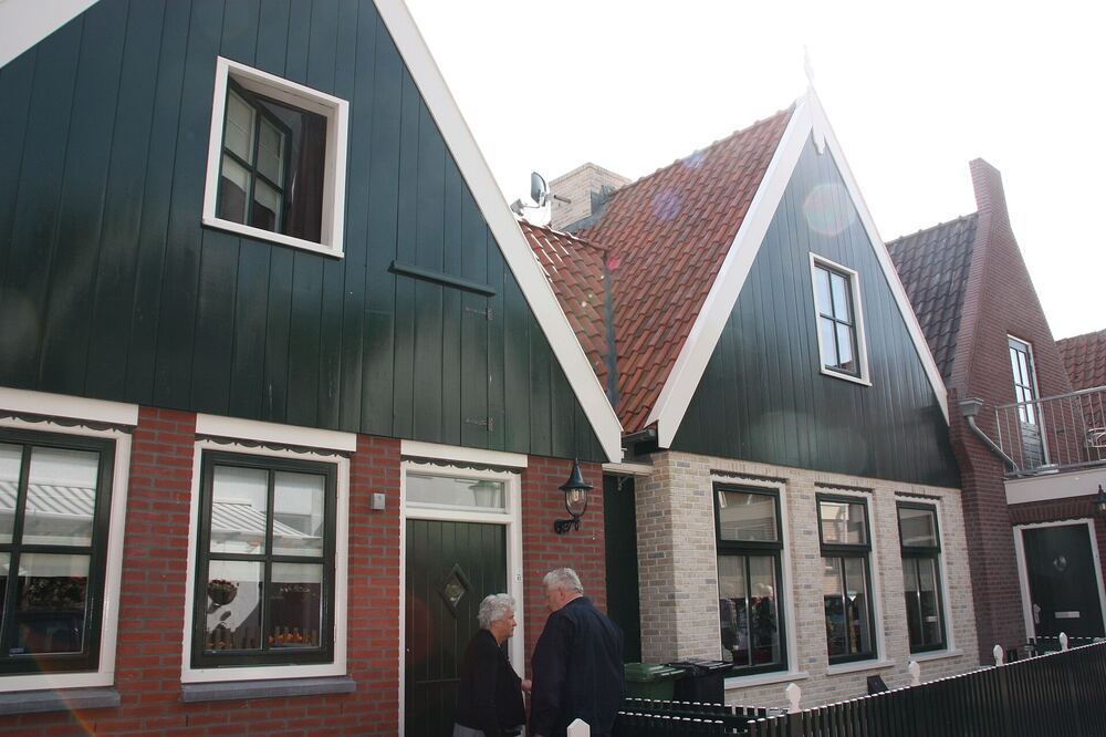 Donkergroen geschilderde houten gevels van oude vissershuisjes in het oude dorp van Urk, met twee mensen die op straat staan te praten